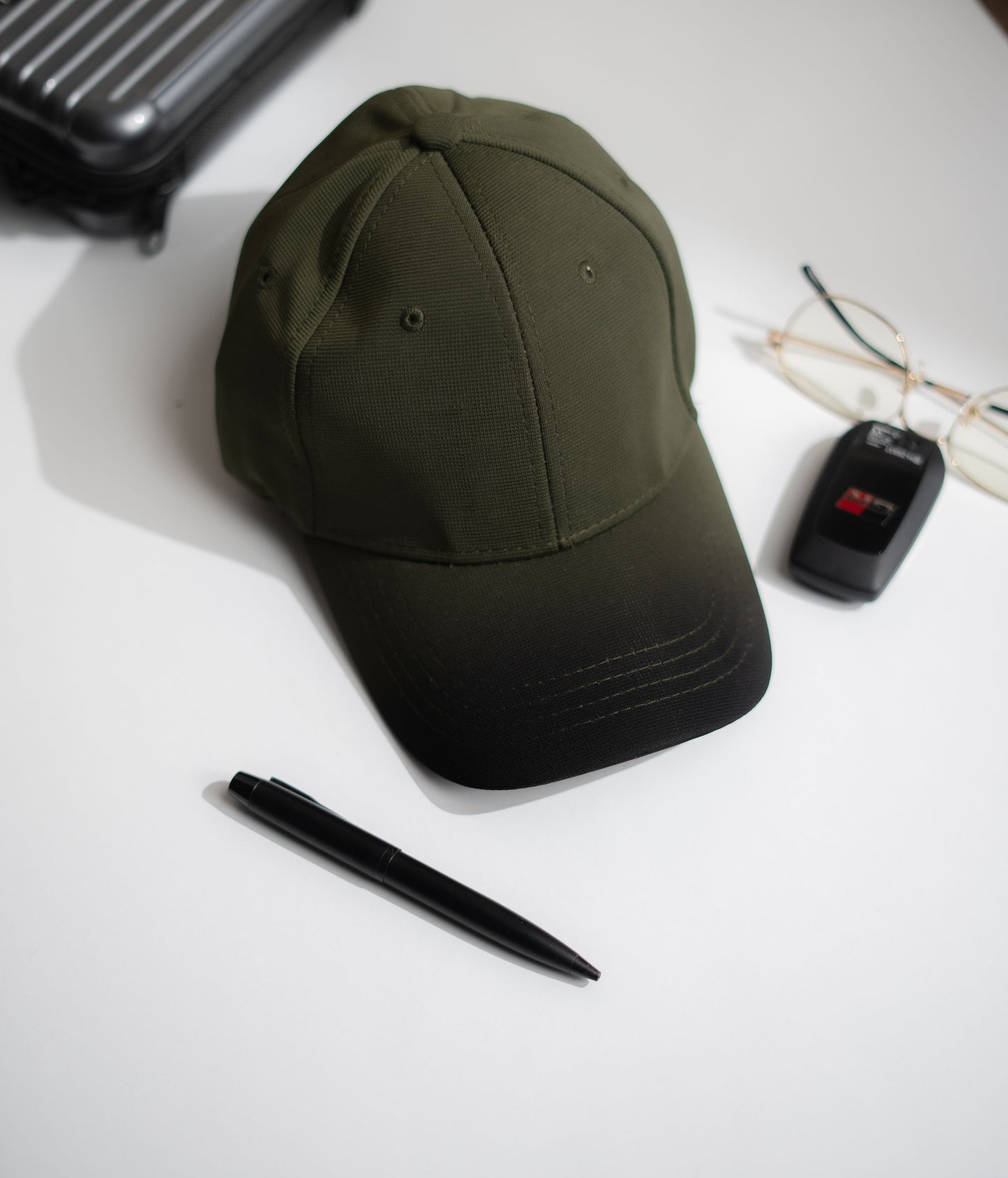 Green cap, pen, and car key fob on a white surface in Pakistan by Caps Nation