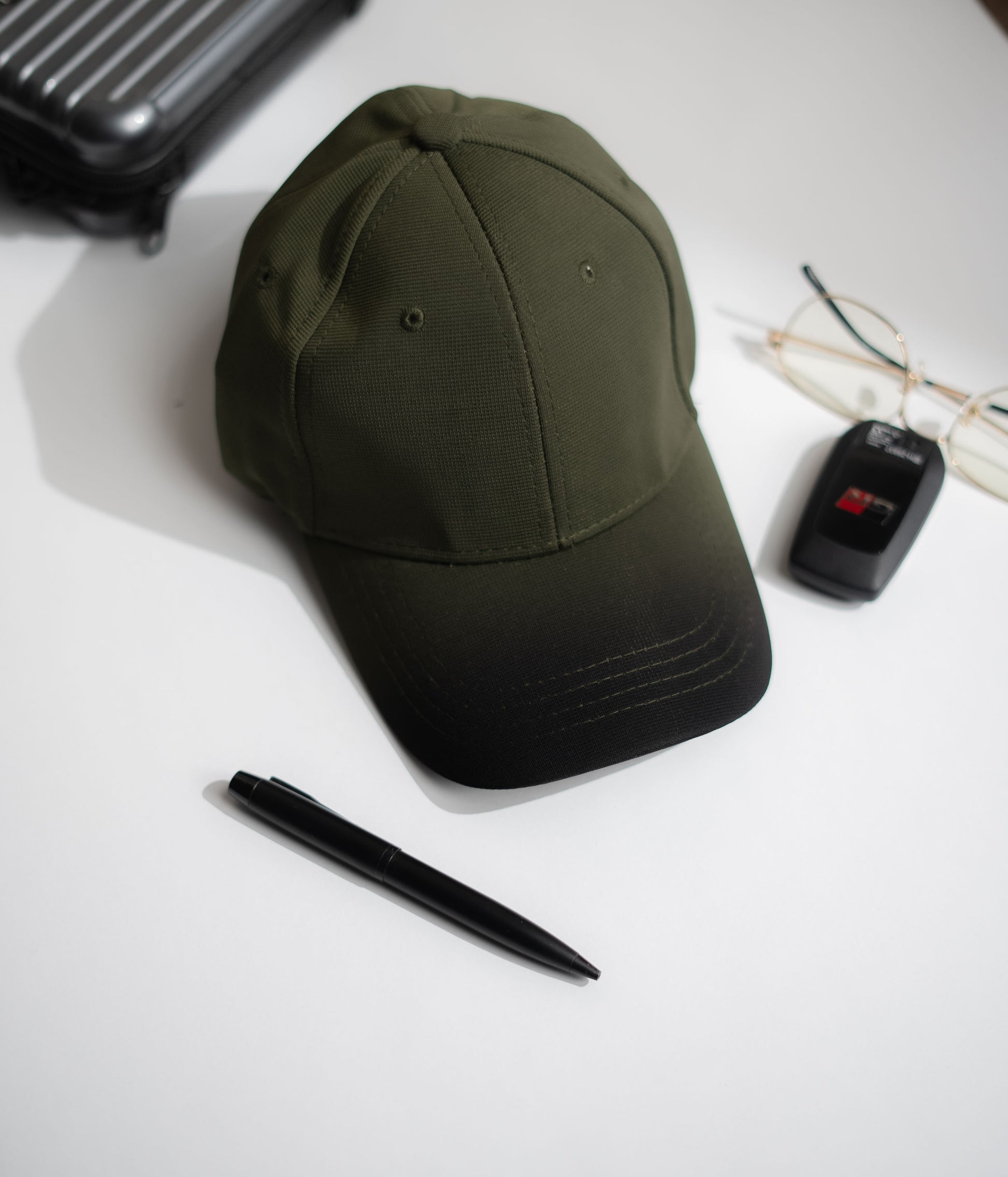Green cap, pen, and car key fob on a white surface in Pakistan by Caps Nation