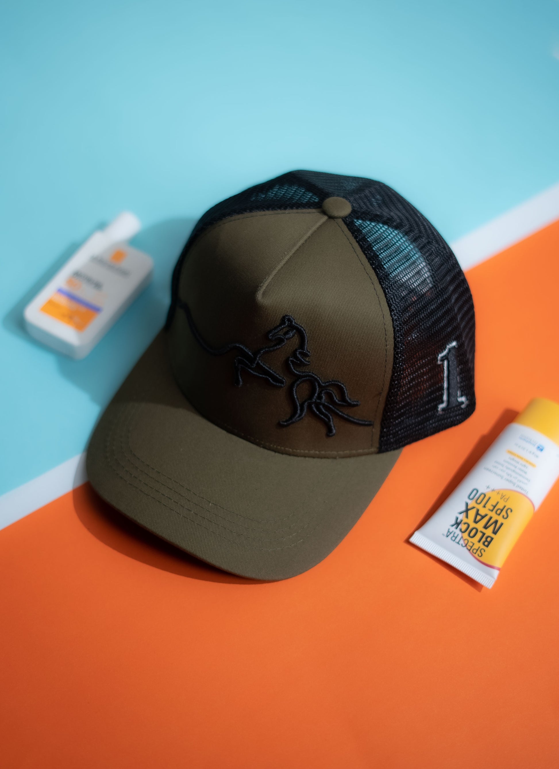 Brown cap with black mesh back on a blue and orange surface with a bottle and packet in Pakistan by Caps Nation