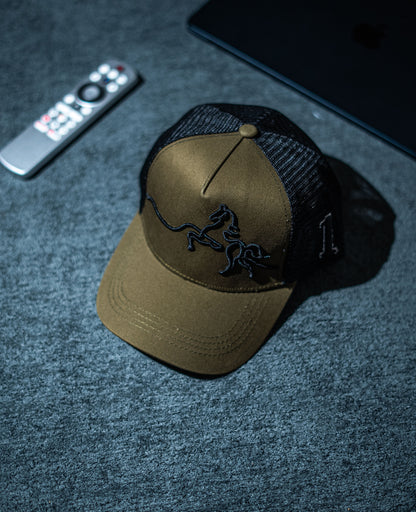 Brown cap with black logo on a dark textured surface with remote control and phone in Pakistan by Caps Nation