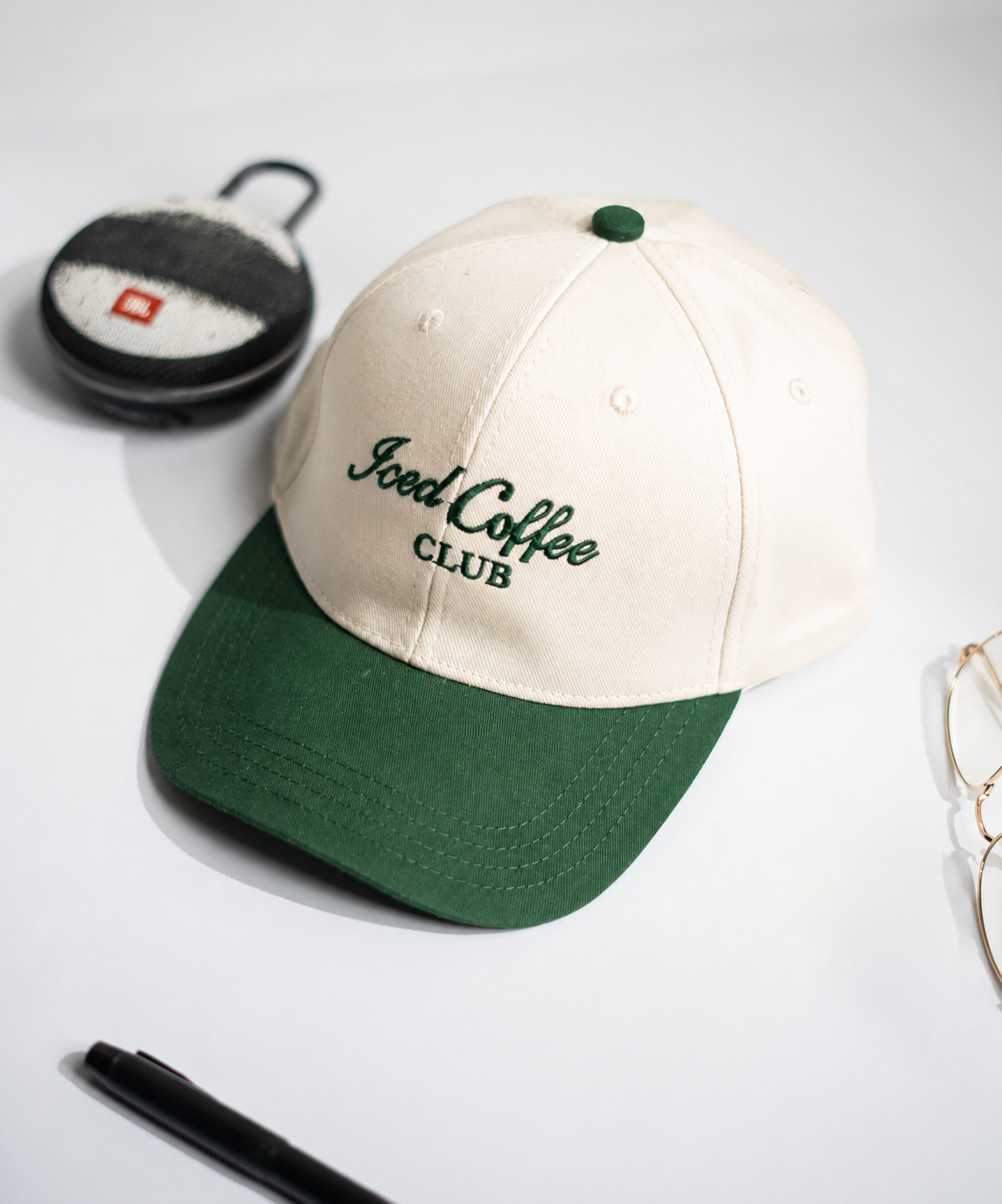 Green and beige cap with 'Good Coffee Club' text on a white surface with a cup and glasses in Pakistan by Caps Nation