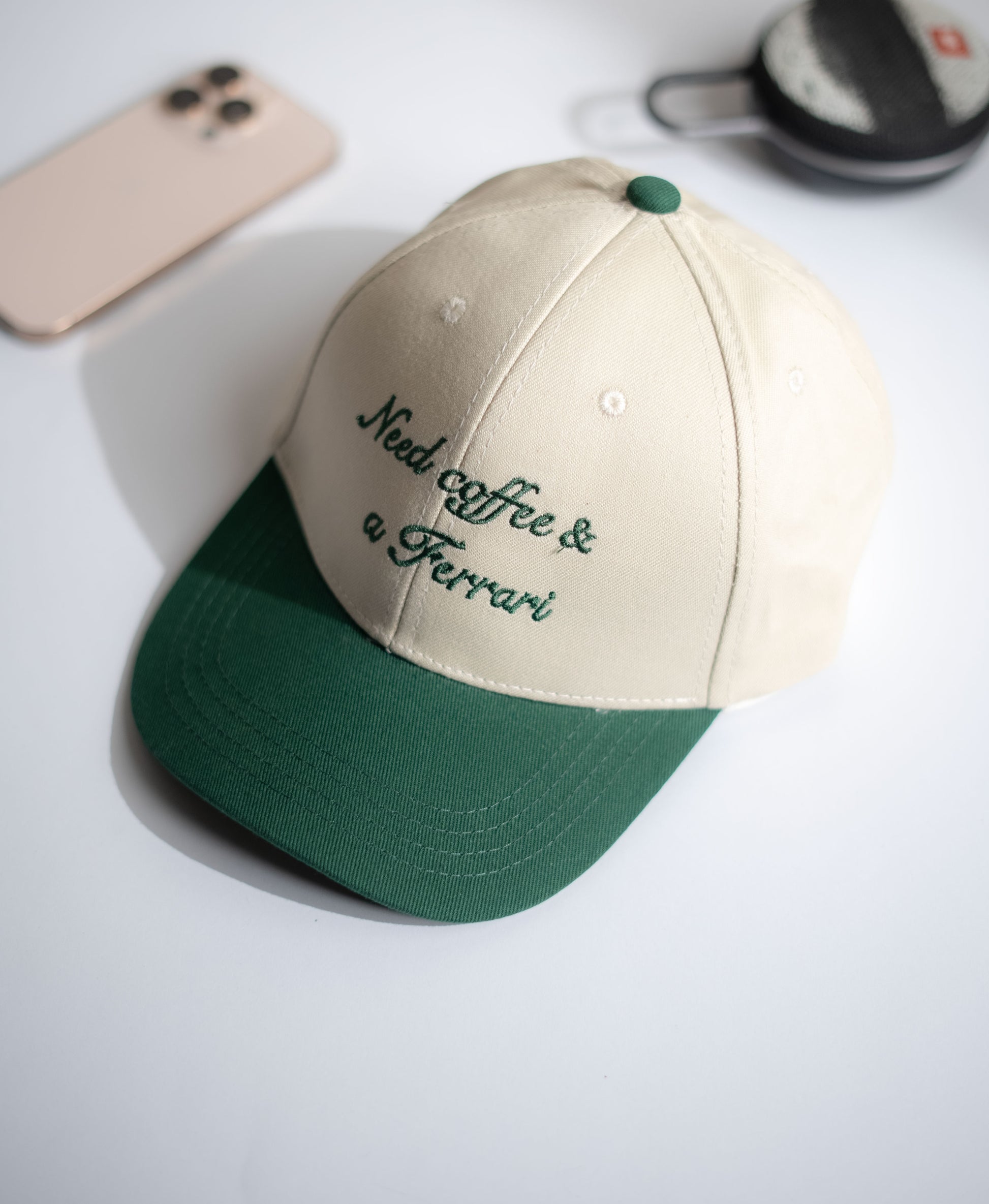 Beige and green cap with 'Need coffee & a Ferrari' text on a white surface in Pakistan by Caps Nation