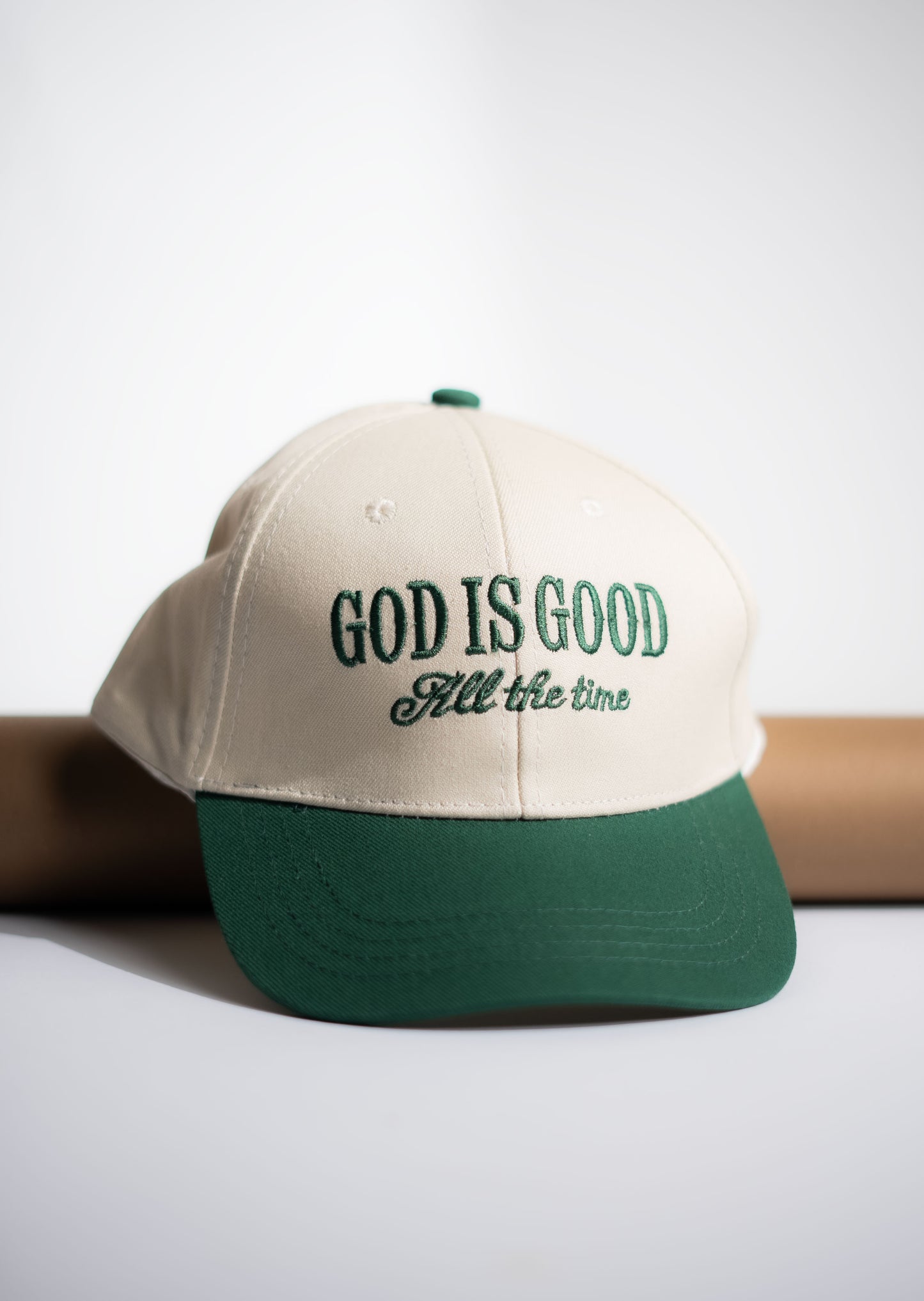 Beige and green cap with 'God is Good All the time' text on a light gray background in Pakistan by Caps Nation