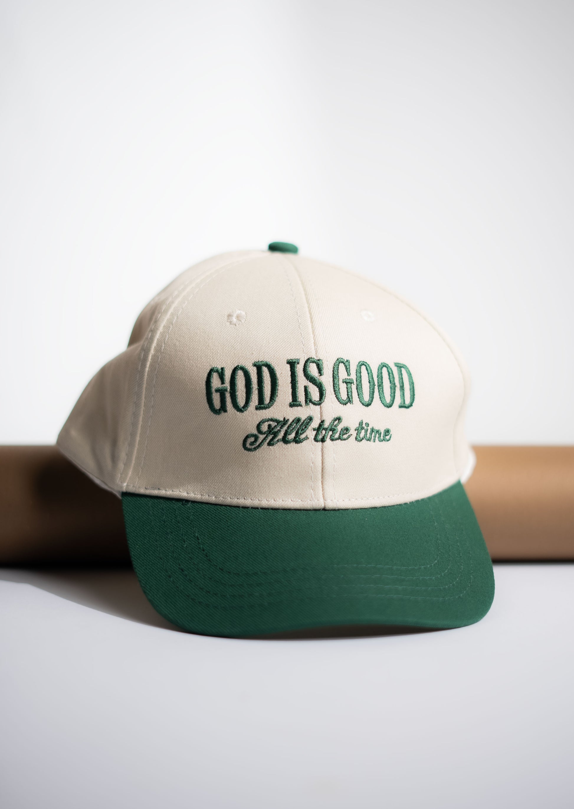 Beige and green cap with 'God is Good All the time' text on a light gray background in Pakistan by Caps Nation