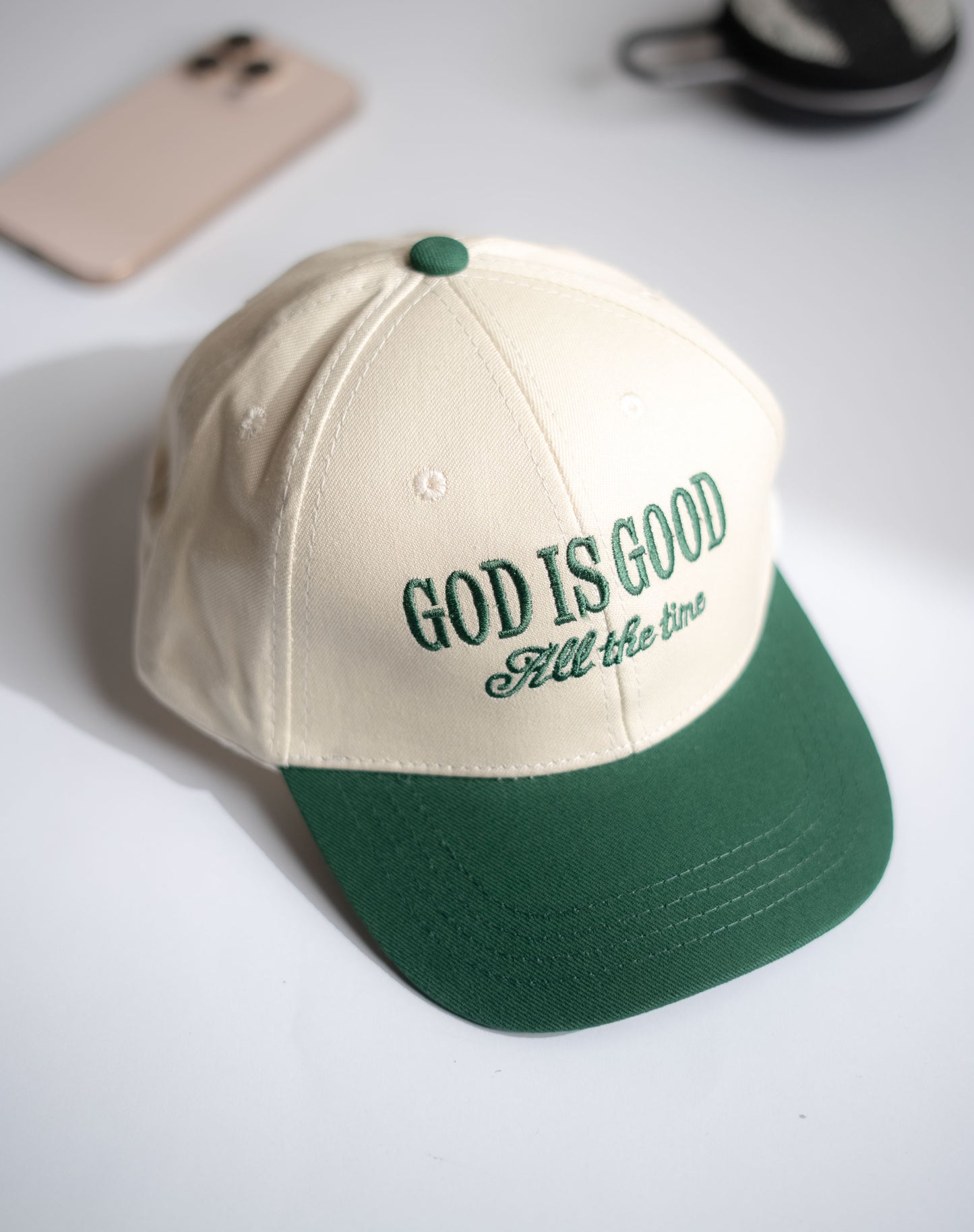 Beige and green cap with 'GOD IS GOOD All the time' text on a white surface in Pakistan by Caps Nation