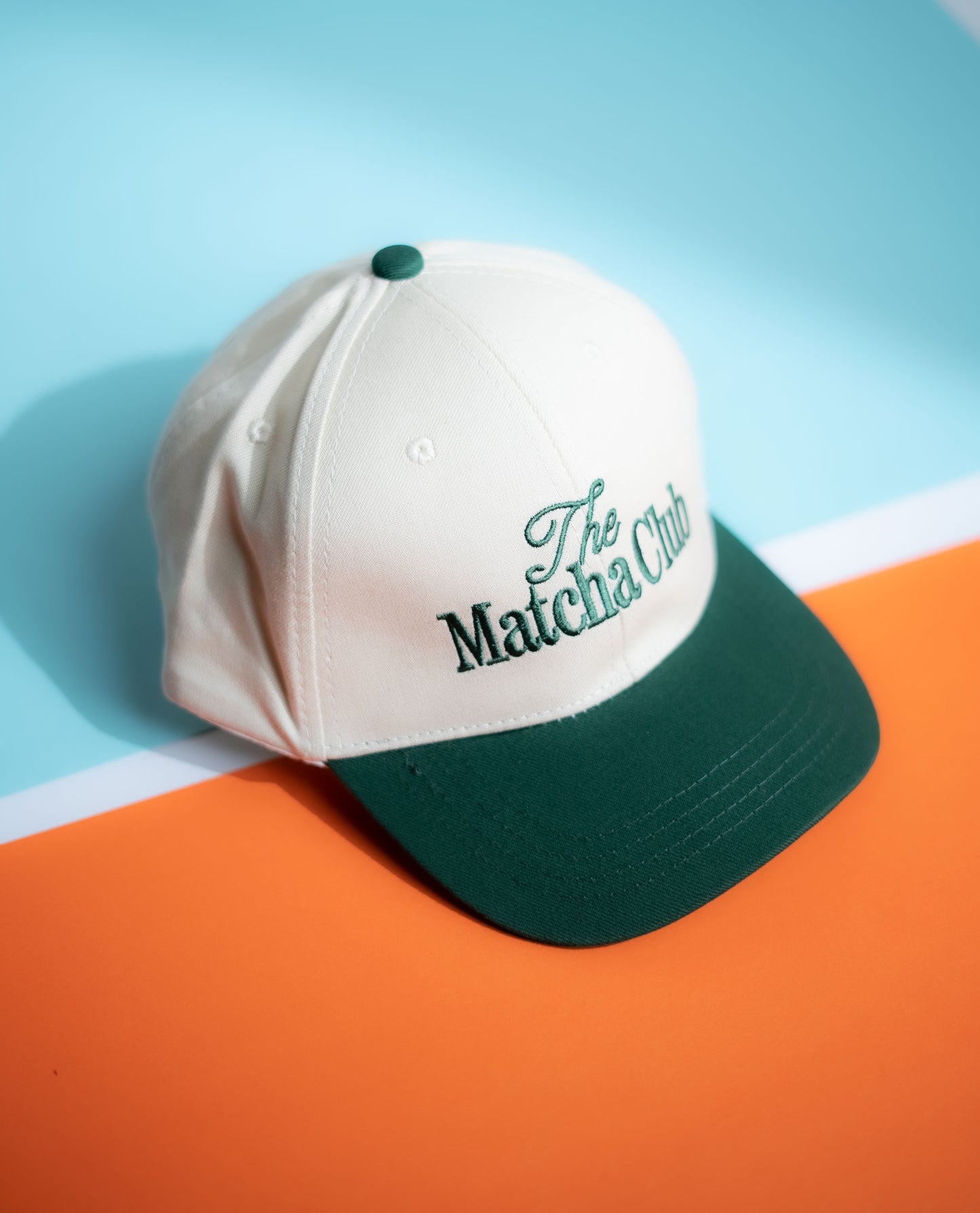 White and green cap with 'The Matcha Club' logo on a blue and orange background in Pakistan by Caps Nation