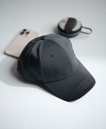 Gray cap on a light gray surface with a phone and small round object in the background in Pakistan by Caps Nation