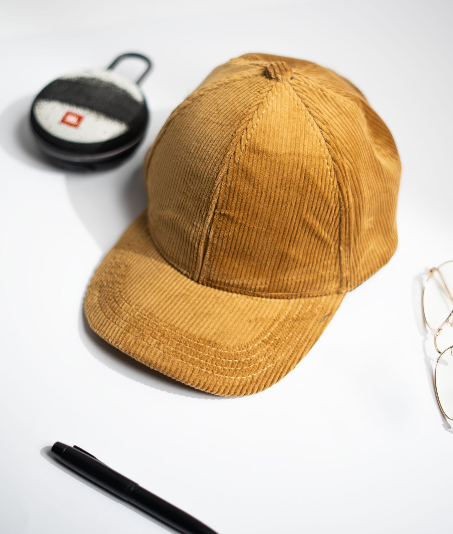 Brown corduroy cap on a white surface with a pen and small  container in Pakistan by Caps Nation