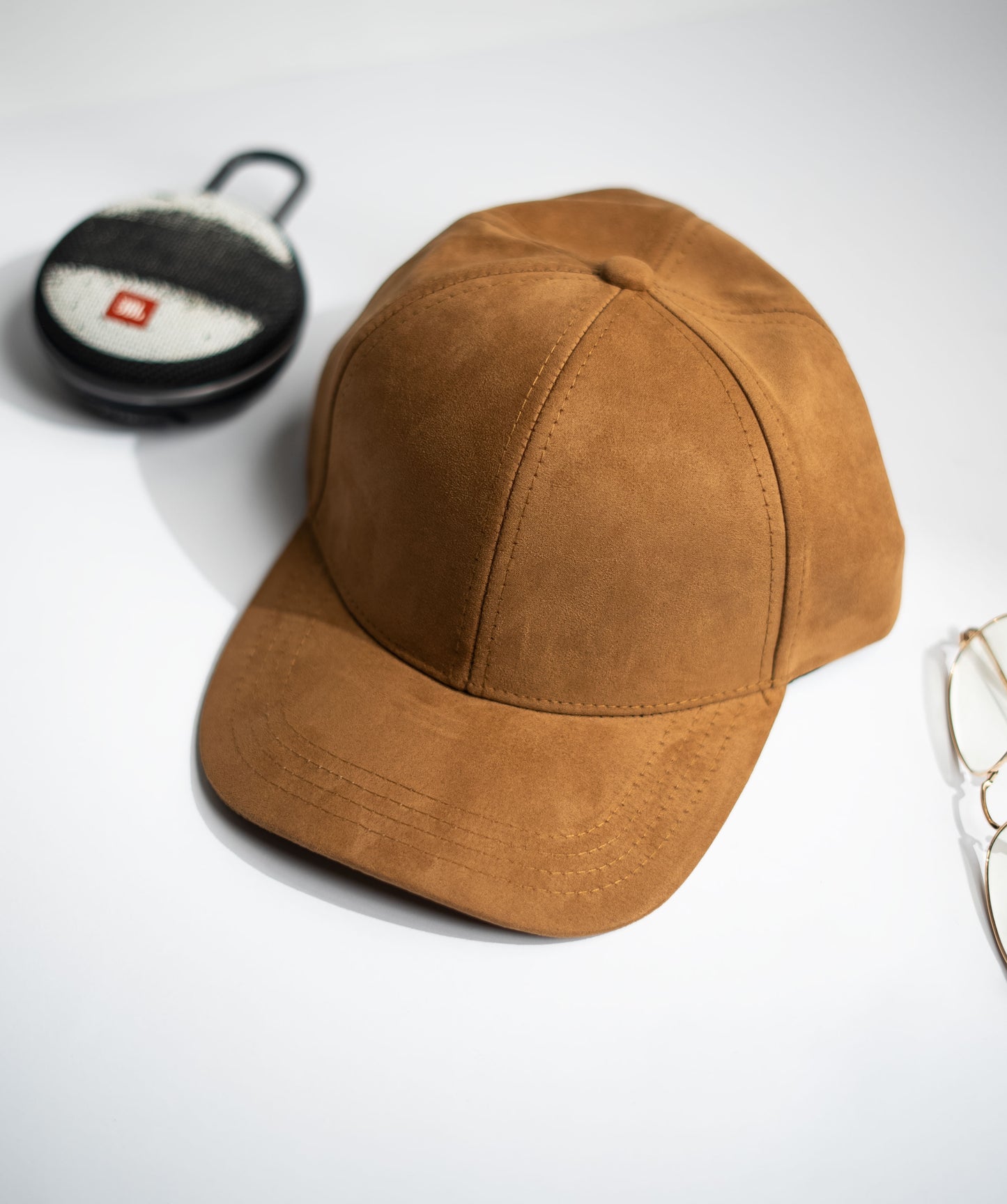 Brown suede cap on a white background with a small round object and glasses in Pakistan by Caps Nation