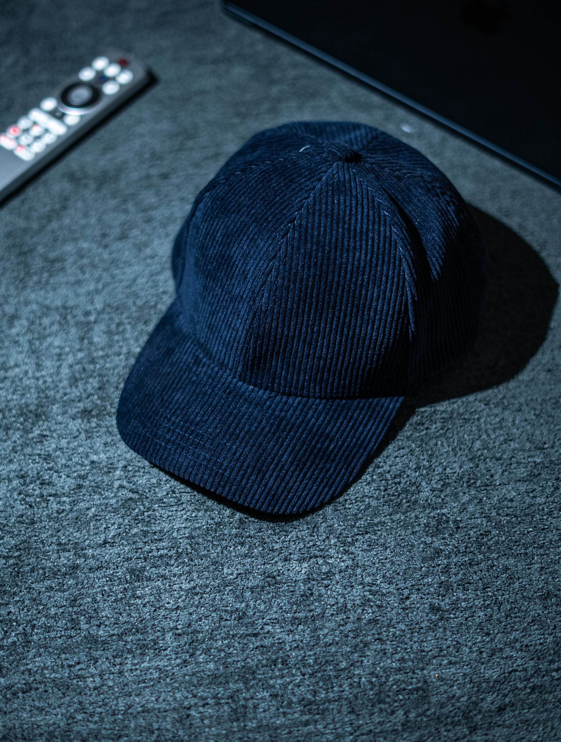 Blue cap on a textured surface with a remote control and electronic device in the background in Pakistan by Caps Nation