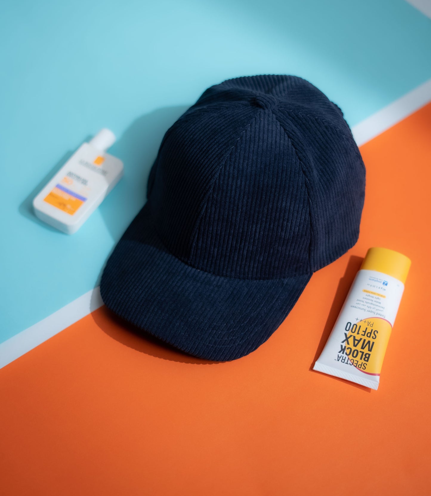 Navy blue cap and sunscreen bottles on a blue and orange background in Pakistan by Caps Nation
