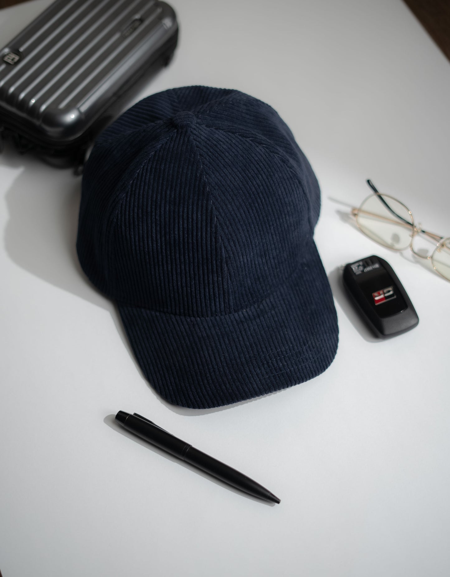 Navy blue cap on a white surface with a pen, small black device, and sunglasses in Pakistan by Caps Nation