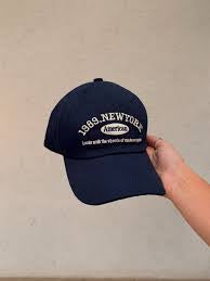 Navy blue cap with white text held against a beige background in Pakistan by Caps Nation