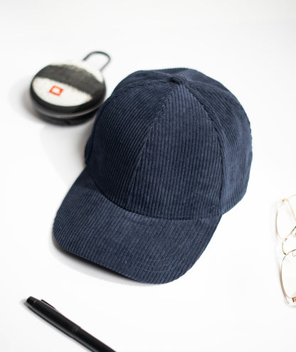 Blue corduroy cap on a white surface with a pen, keychain, and glasses. in Pakistan by Caps Nation