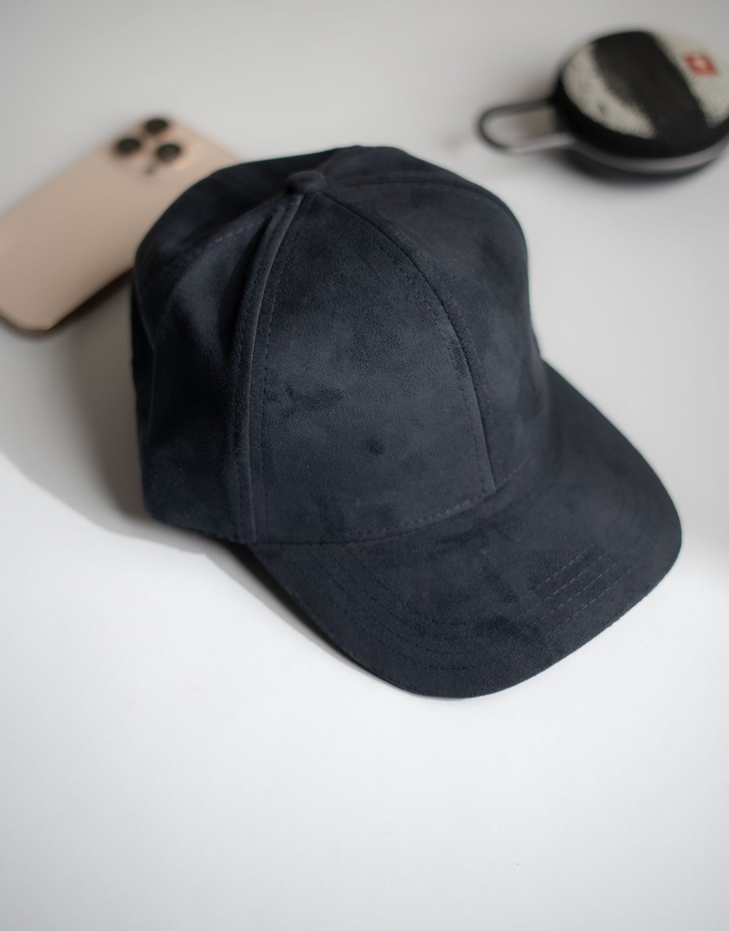 Black cap on a white surface with a phone and small container in the background in Pakistan by Caps Nation