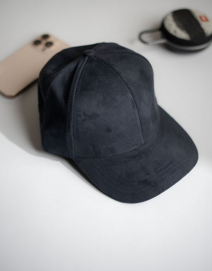 Black cap on a white surface with a phone and small container in the background in Pakistan by Caps Nation
