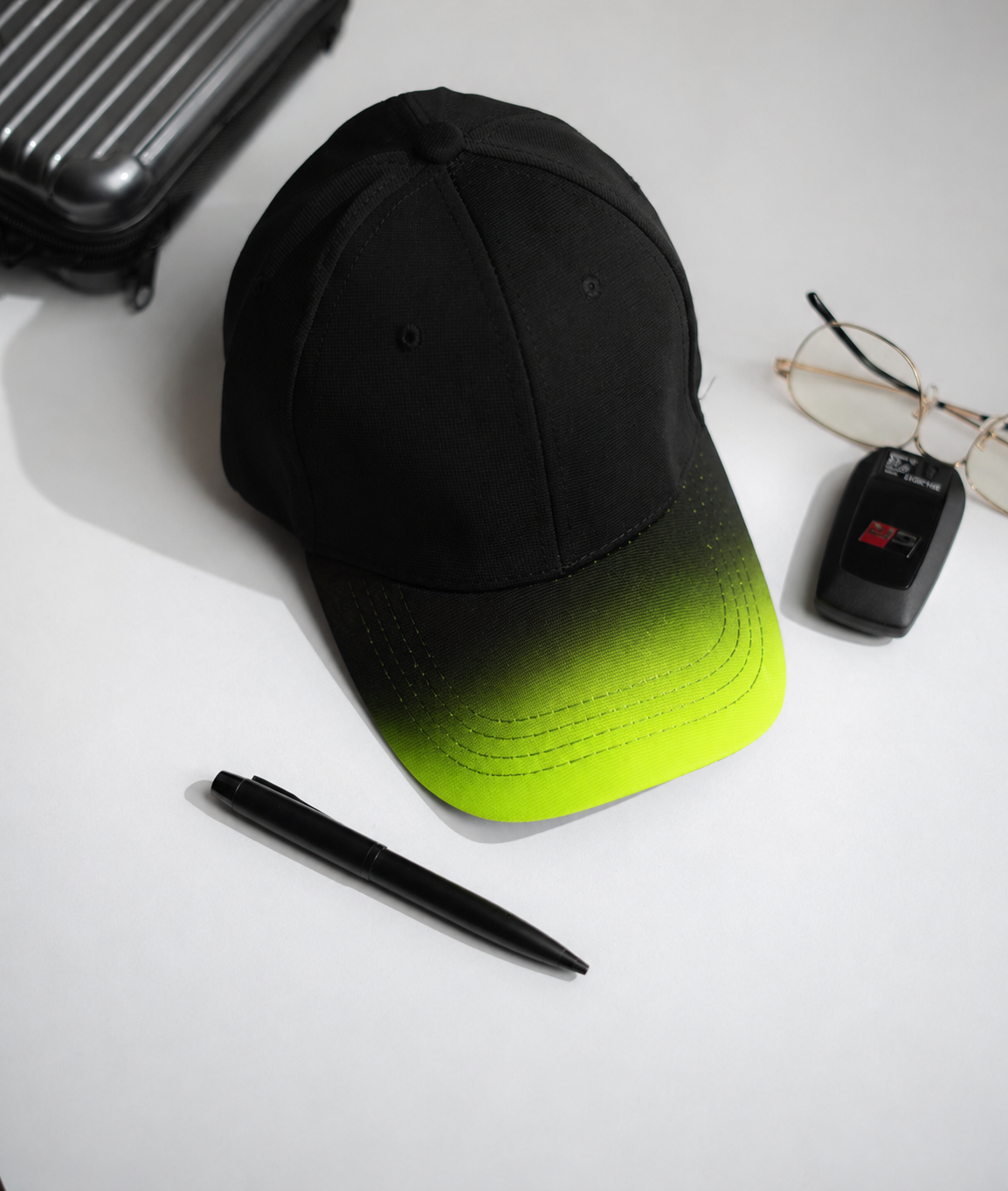 Black and green gradient cap with a pen, glasses, and suitcase on a white surface in Pakistan by Caps Nation