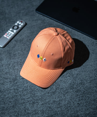 Brown cap with embroidered pins on a dark textured surface with a remote control and electronic device in Pakistan by Caps Nation