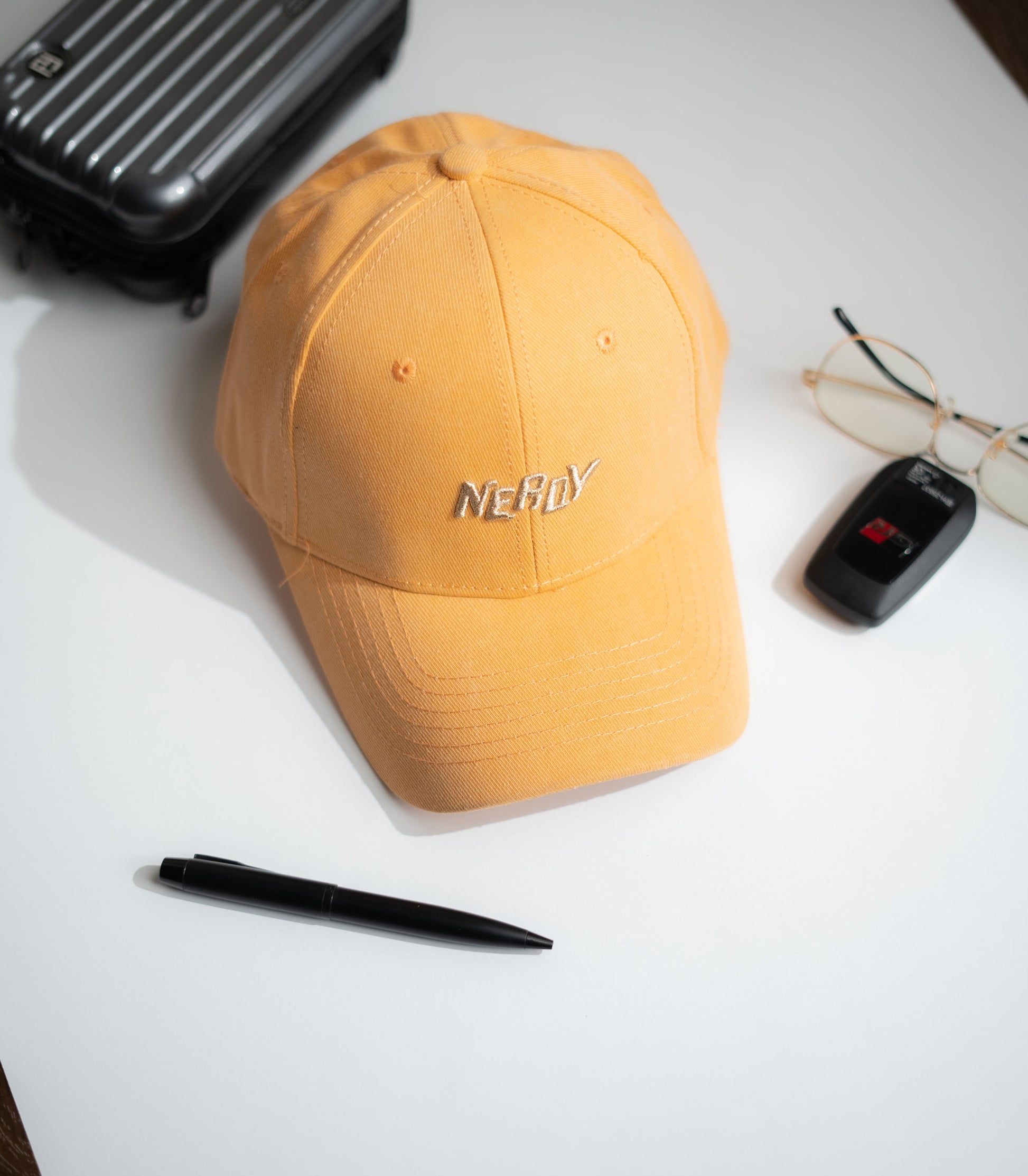 Yellow cap with 'NERDY' text on a white surface with a pen, glasses, and suitcase in Pakistan by Caps Nation