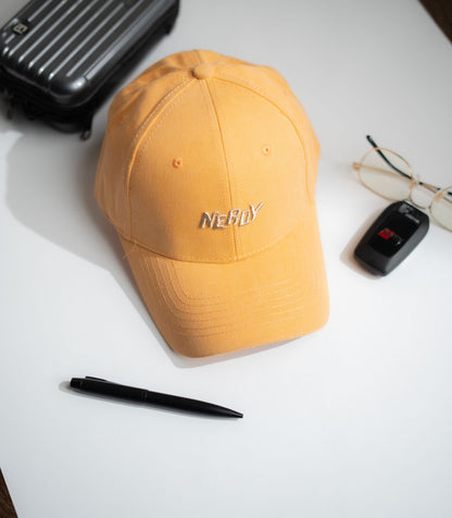 Yellow cap with 'NERDY' text on a white surface with a pen, glasses, and suitcase in Pakistan by Caps Nation