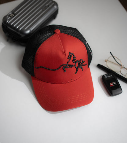 Red and black cap with a logo on a white surface with a car key and glasses in Pakistan by Caps Nation