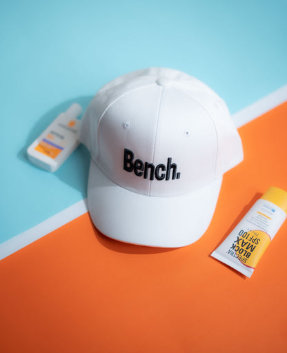 White cap with 'Bench' logo on a blue and orange background in Pakistan by Caps Nation