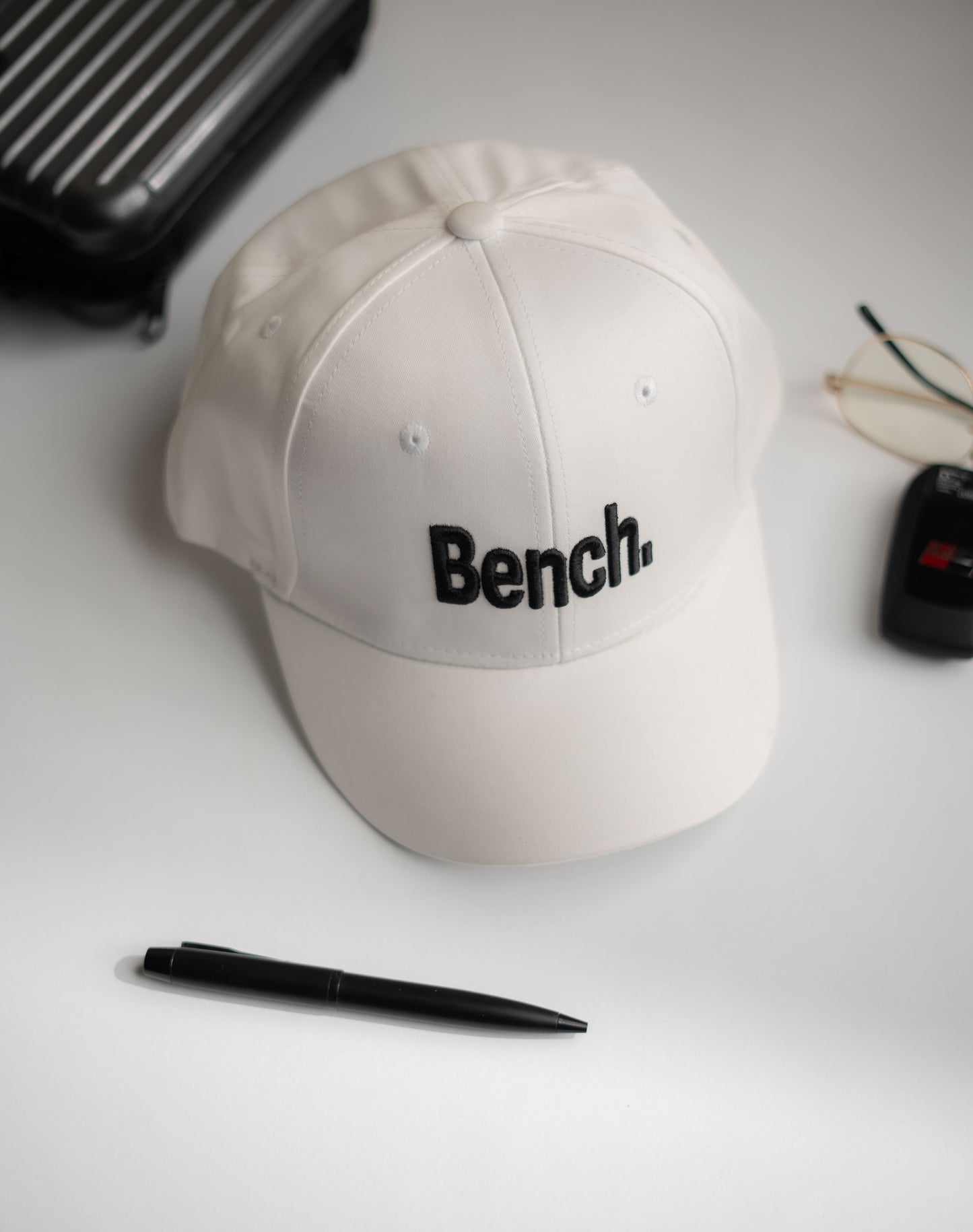 Beige cap with 'Bench' logo on a white surface with a pen and glasses in Pakistan by Caps Nation