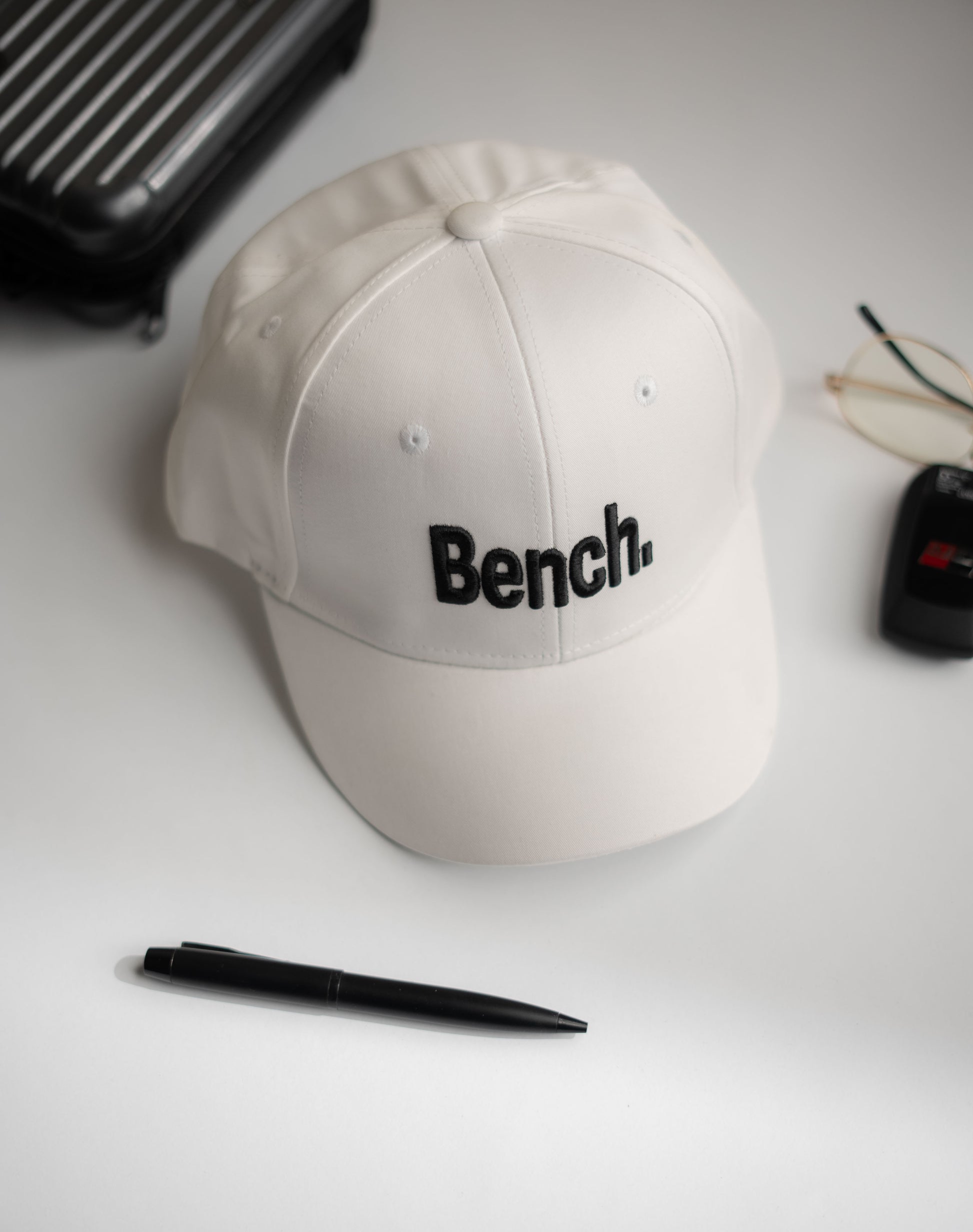 Beige cap with 'Bench' logo on a white surface with a pen and glasses in Pakistan by Caps Nation
