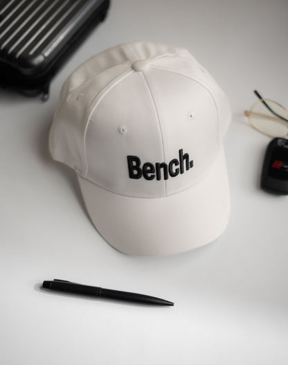 Beige cap with 'Bench' logo on a white surface with a pen and glasses in Pakistan by Caps Nation