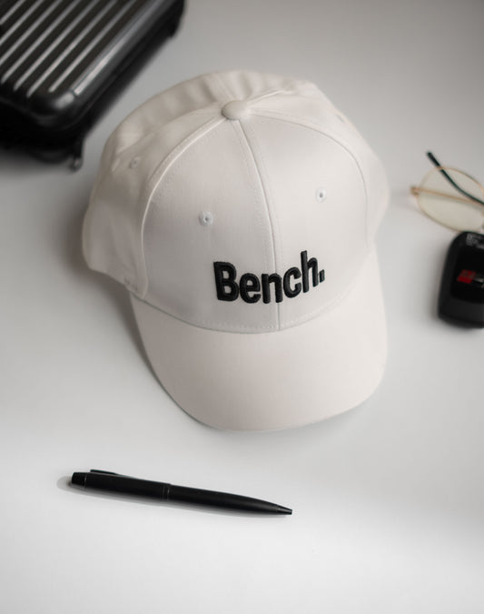 Beige cap with 'Bench' logo on a white surface with a pen and glasses in Pakistan by Caps Nation