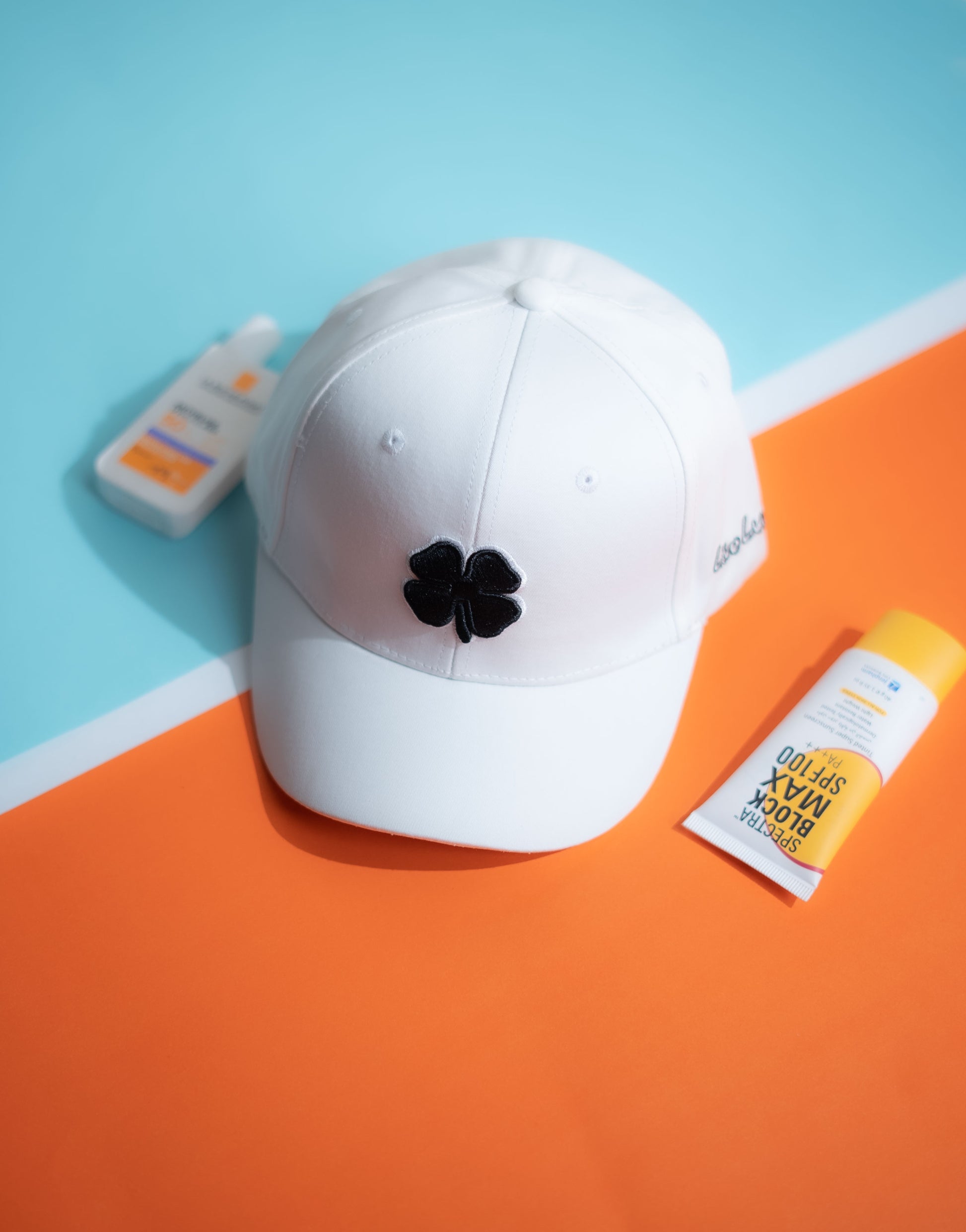 White cap with a black clover design on an orange and blue background in Pakistan by Caps Nation