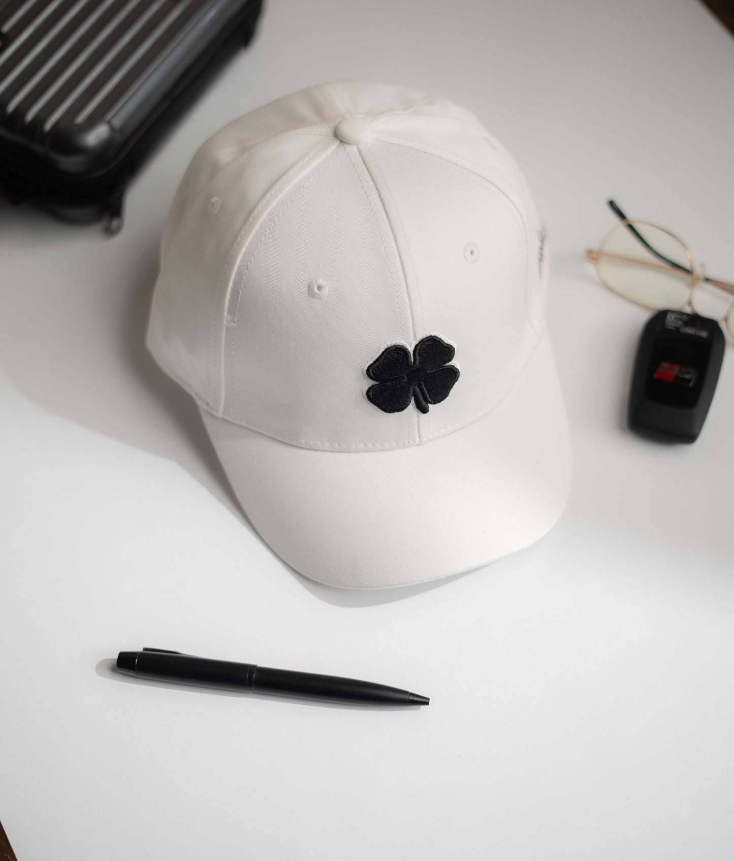 White cap with black flower emblem on a white surface with a pen and small black device in Pakistan by Caps Nation