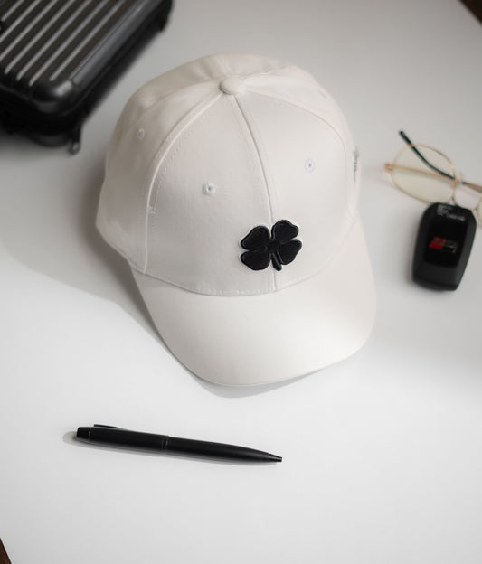 White cap with black flower emblem on a white surface with a pen and small black device in Pakistan by Caps Nation