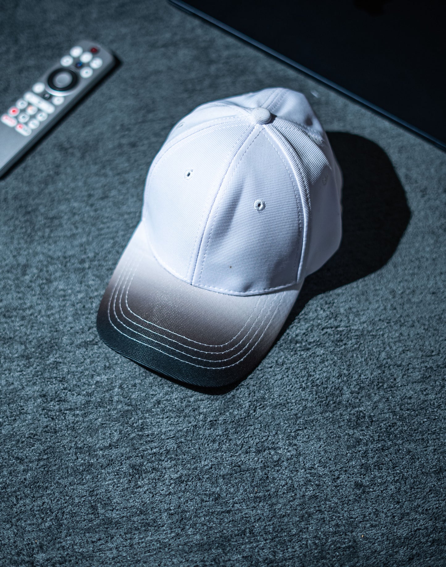 White cap on a dark textured surface with a remote control in the background in Pakistan by Caps Nation