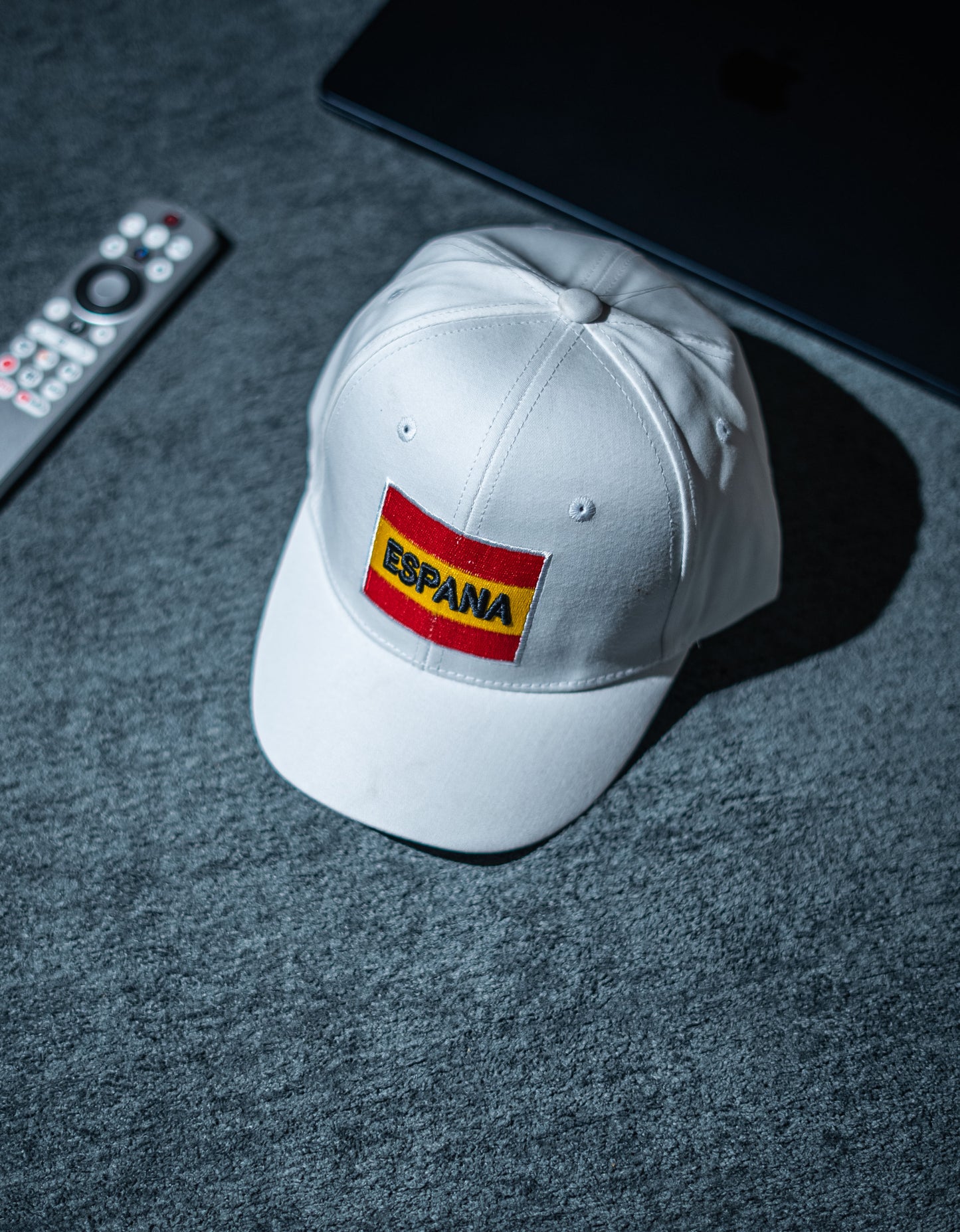 White cap with 'ESPAñA' logo on a dark surface in Pakistan by Caps Nation